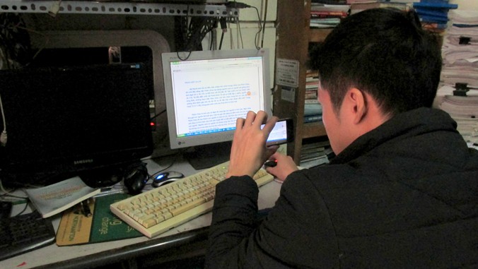 Một sinh viên đang thực hiện công đoạn sao chép kiến thức trong quán phô-tô bằng điện thoại. Ảnh: Nguyễn Hoan