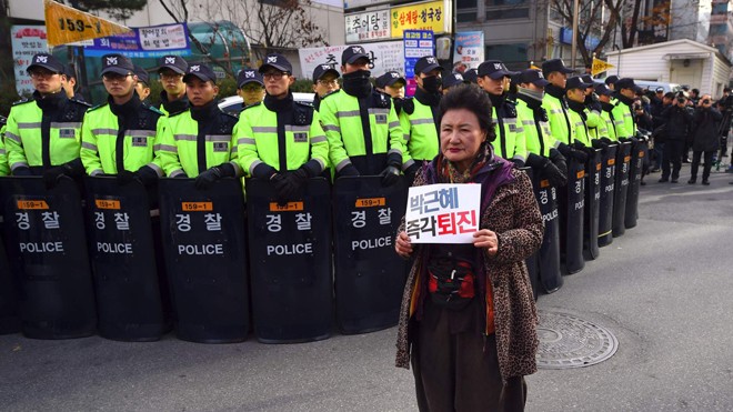 Một người biểu tình Hàn Quốc đứng trước trụ sở đảng Saenuri cầm quyền giơ tấm biển ghi “Bà Park Geun-hye, hãy từ chức!”. Ảnh: Jiji