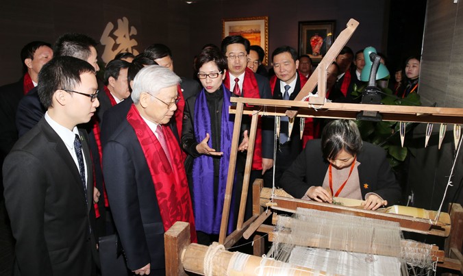 Tổng Bí thư Nguyễn Phú Trọng xem chế tác sản phẩm tơ lụa của Tập đoàn Vạn Sự Lợi. Ảnh: TTXVN