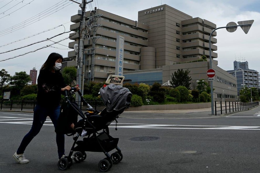 Một người phụ nữ đeo khẩu trang đẩy xe trẻ em bên ngoài Bệnh viện Juso, thành phố Osaka