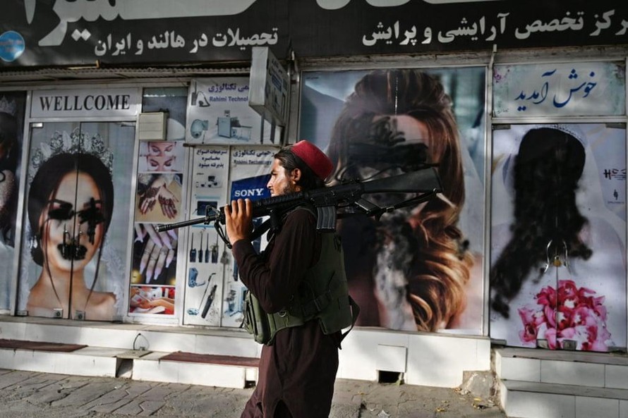 Một lính Taliban đi tuần ở Kabul. Đằng sau, các hình ảnh quảng cáo phụ nữ đã bị xóa bỏ