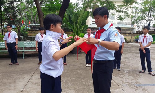Thầy Nguyễn Hữu Trí hướng dẫn đội viên đeo khăn quàng đỏ. Ảnh: NVCC