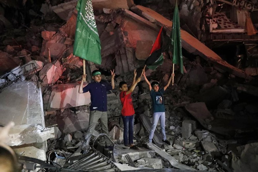 Trẻ em Palestine vẫy cờ Palestine và Hamas khi đang đứng trên đống đổ nát để bày tỏ vui mừng với thỏa thuận ngừng bắn ở Gaza ngày 21/5. Ảnh: AP