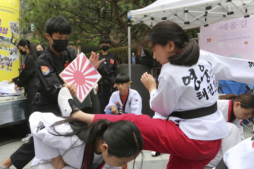 Học sinh Hàn Quốc đá một tấm bảng gỗ có in cờ Nhật Bản trong một cuộc tuần hành ở Seoul Ảnh: AP