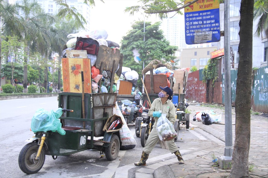 Công nhân môi trường và xe rác cao quá đầu người trên phố Hà Nội. Nếu không chất thêm rác lên, họ sẽ không kịp giờ thu dọn rác. Ảnh: Trường Phong