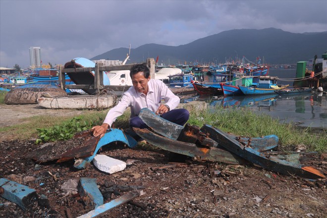 Ngư dân Lê Văn Hưởng bên xác ghe máy vừa được tiêu hủy bên “nghĩa địa” tàu cá. Ảnh: Nguyễn Thành 