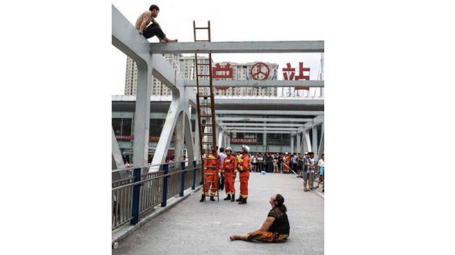 Ông Xue Yan ngồi vắt vẻo trên thành cầu trong khi vợ ở dưới hết lời khuyên nhủ ông trèo xuống. Ảnh: Biglawnewsline