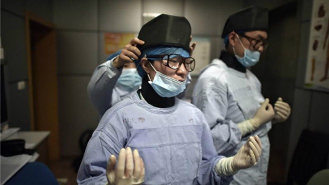 Đồng nghiệp giúp Liu Ya mặc đồ bảo hộ trước giờ phẫu thuật. Ảnh: China Daily.