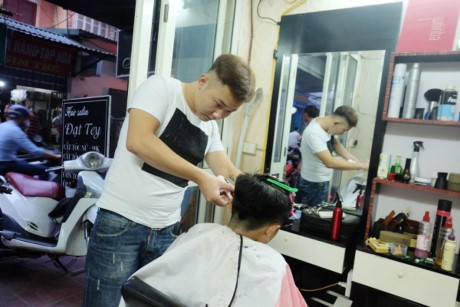 Khánh bận rộn cắt tóc cho khách ở một cửa hiệu trên đường Đê La Thành, Đống Đa, Hà Nội.