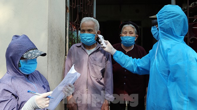 Cán bộ y tế đến từng nhà dân ở thôn Hạ Lôi, Mê Linh, Hà Nội đo thân nhiệt và ghi nhận tình hình sức khỏe từng người dân. Ảnh: Mạnh Thắng