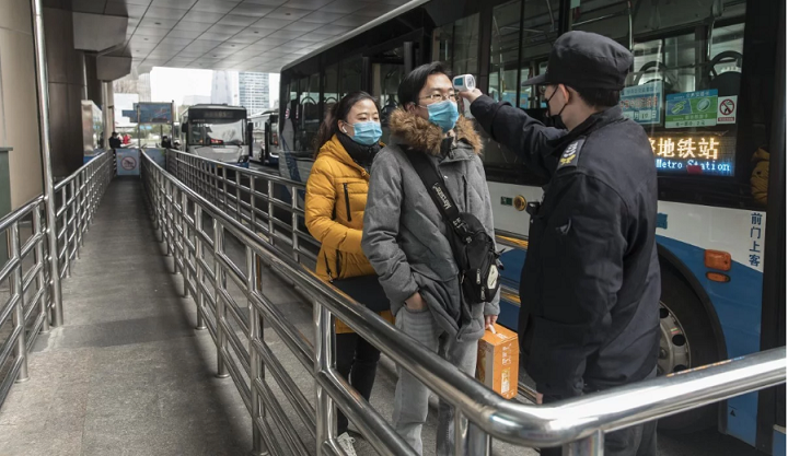 Một quan chức kiểm tra nhiệt độ của hành khách tại một bến xe buýt ở Thượng Hải. Ảnh: Bloomberg