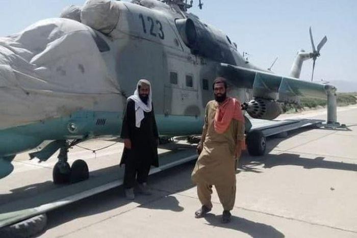 Hai tay súng Taliban đang đứng trước chiếc trực thăng vũ trang Mi-35.