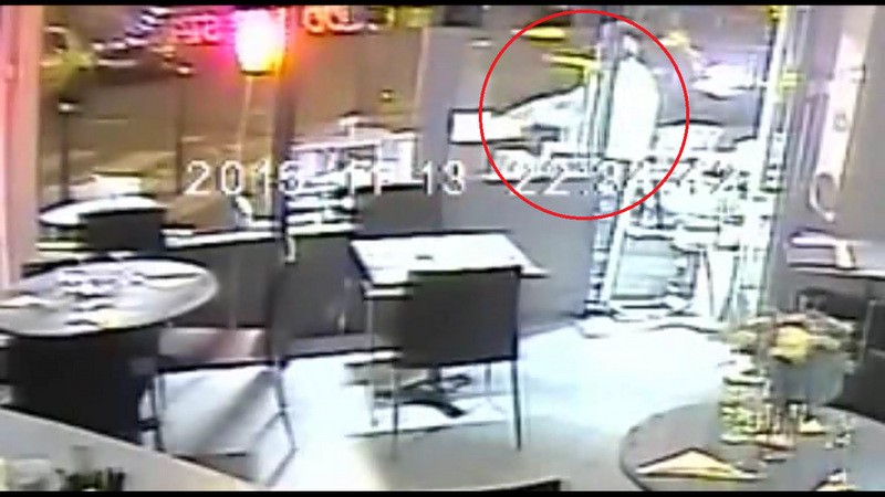 Kẻ khủng bổ (khoanh tròn đỏ) chĩa thẳng súng vào đầu một người phụ nữ trốn dưới gầm bàn, nhưng súng của hắn bất ngờ bị kẹt đạn.