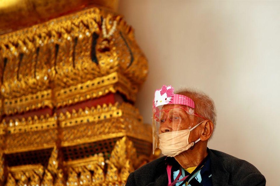 Một cụ ông đeo khẩu trang và tấm chắn ngồi trong một ngôi đền ở Bangkok. Ảnh: Reuters