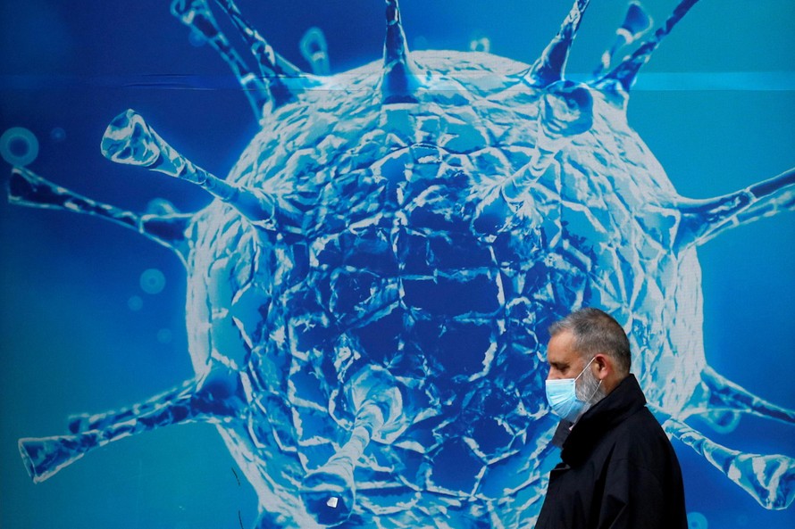Một người đàn ông đeo khẩu trang đi qua tấm áp phích in hình virus corona ở Oldham, Anh. Ảnh: Reuters