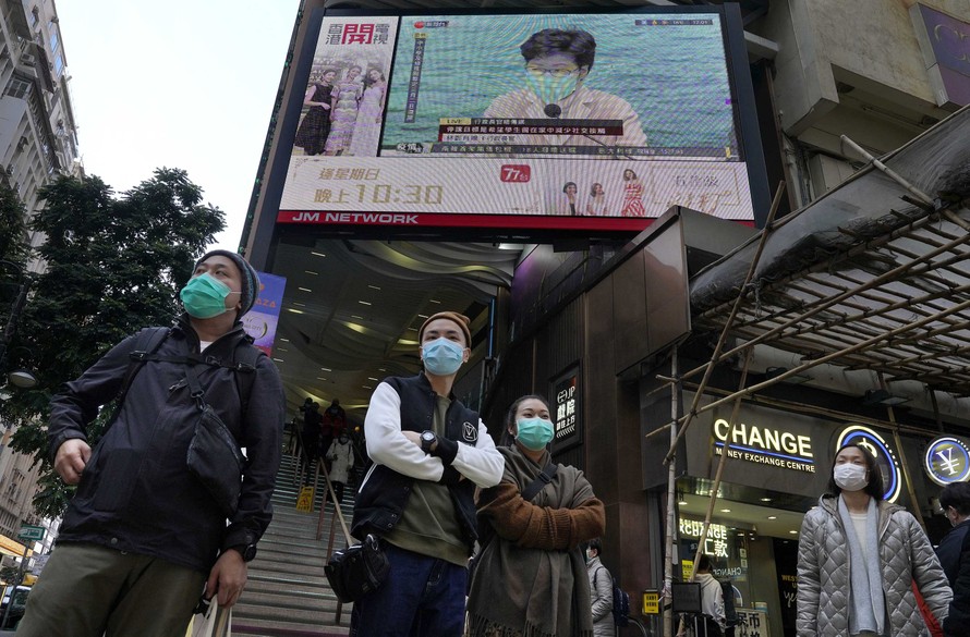 Người dân Hong Kong đeo khẩu trang đứng trước màn hình TV chiếu hình ảnh bà Carrie Lam. Ảnh: AP.