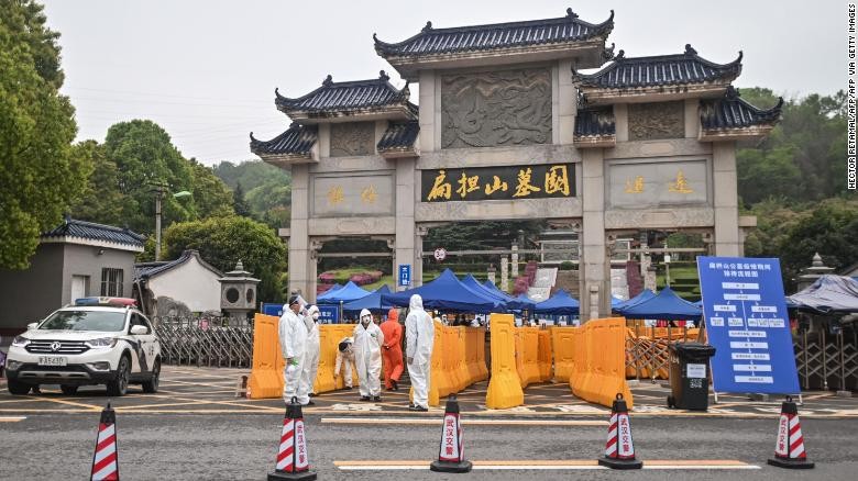 Người đàn ông đeo khẩu trang, mặc áo mưa xanh ôm ảnh người thân bên ngoài nghĩa trang Biandanshan ở Vũ Hán hôm 31/3. Ảnh: Getty.