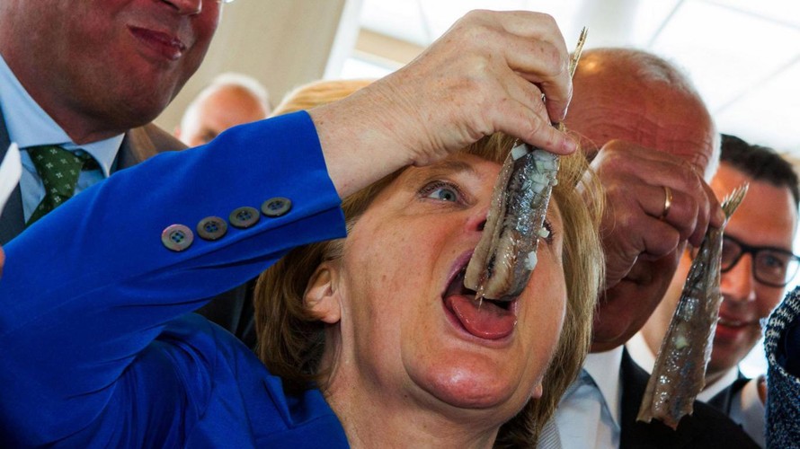 Thủ tướng Đức Angela Merkel há miệng ăn cá trích ngâm sau lễ đặt tên cho chiếc tàu đánh cá ROS 777 của trại nuôi cá Warnemuender ở Sassnitz, miền đông nước Đức hôm 26/5