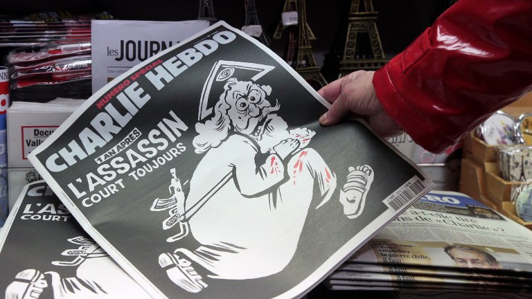 Một người Pháp cầm trên tay số báo đặc biệt của Charlie Hebdo phát hành ngày hôm nay kỉ niệm 1 năm vụ khủng bố tòa soạn. Ngoài trang bìa là dòng chữ "Một năm sau: Kẻ giết người vẫn còn đó".