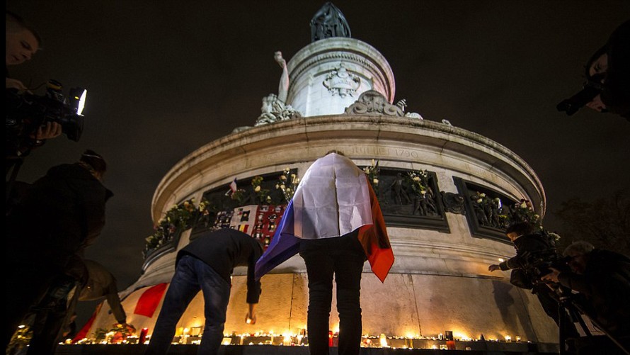 Một người dân khoác lá cờ Pháp đặt nến tưởng nhớ những nạn nhân xấu số trong vụ khủng bố Paris tại quảng trường Republique tối ngày 13/11/2016.