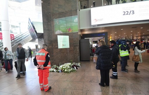 Nhân viên sân bay và hành khách đứng trước biển tưởng niệm nạn nhân thiệt mạng trong vụ khủng bố tại sân bay quốc tế Brussels hôm 22/3.