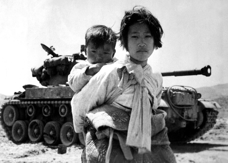 Bé gái Triều Tiên cõng em đi qua một chiếc xe tăng M-26 tại Haengju, Hàn Quốc, ngày 9/6/1951.