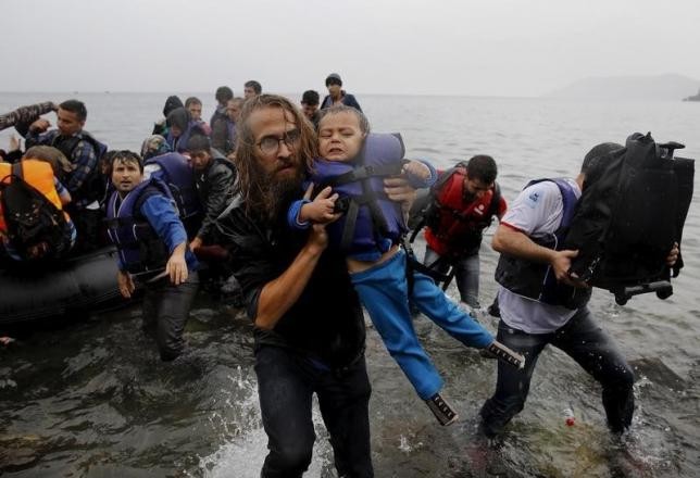 Một tình nguyện viên bế trẻ tị nạn Syria sau khi những người di cư vượt qua biển Aegean từ Thổ Nhĩ Kỳ tới đảo Lesbos, Hy Lạp hôm 23/9/2015. Ảnh: Reuters