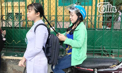 Người mẹ ngồi trên xe máy thắt bím cho con gái trước cổng trường.