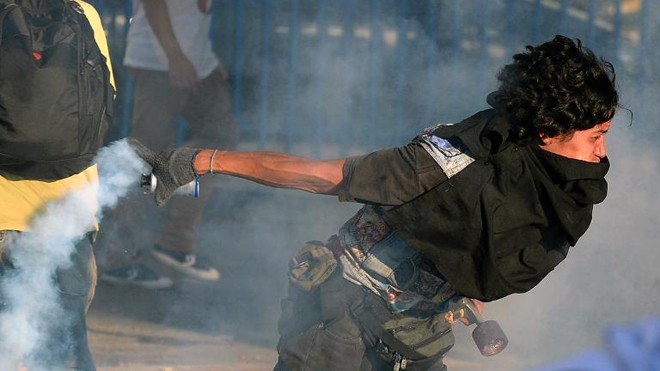 Một người biểu tình Venezuela trả lựu đạn cay về phía cảnh sát. Ảnh: Juan Barreto
