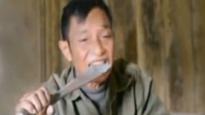 Ông Đinh Mỳ ngậm lưỡi dao nung đỏ vừa lấy ra từ bếp. 