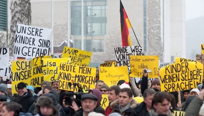 Người biểu tình mang theo các biểu ngữ phản đối, tập trung bên ngoài dinh Thủ tướng Đức Angela Merkel hồi cuối tuần trước. Ảnh: BBC.