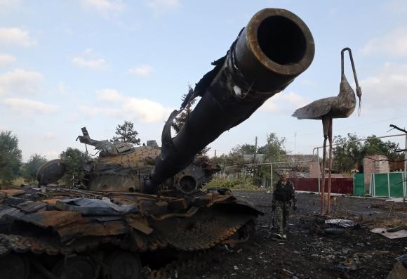 Một tay súng ly khai bước bên cạnh xác chiếc xe tăng ở Donetsk hôm 28/8