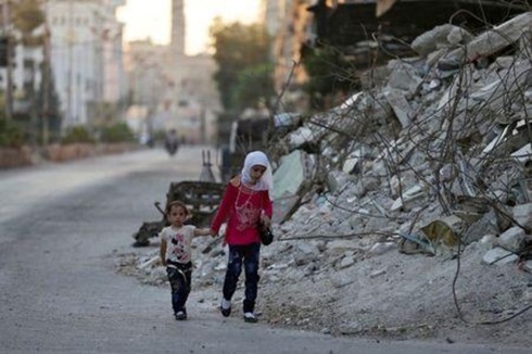 Hai trẻ em đi bộ qua một tòa nhà đổ nát trong ngày lễ Eid al-Fitr tại khu phố Douma, Damascus, Syria. Ảnh: Reuters.