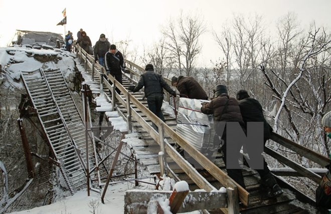 Người dân đi qua chốt kiểm soát giữa quân đội Ukraine và lực lượng đòi độc lập bằng chiếc thang gỗ thay thế cho chiếc cầu bị phá hủy trong một đợt giao tranh ở khu vực Luhansk ngày 16/12. (Nguồn: EPA/TTXVN)