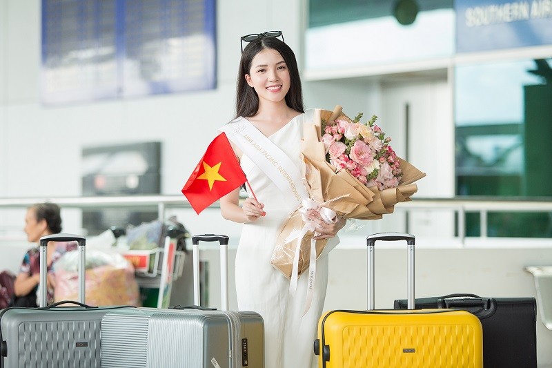 Hoa khôi Huỳnh Thúy Vi cầm hoa và cờ Việt Nam trước giờ lên máy bay.